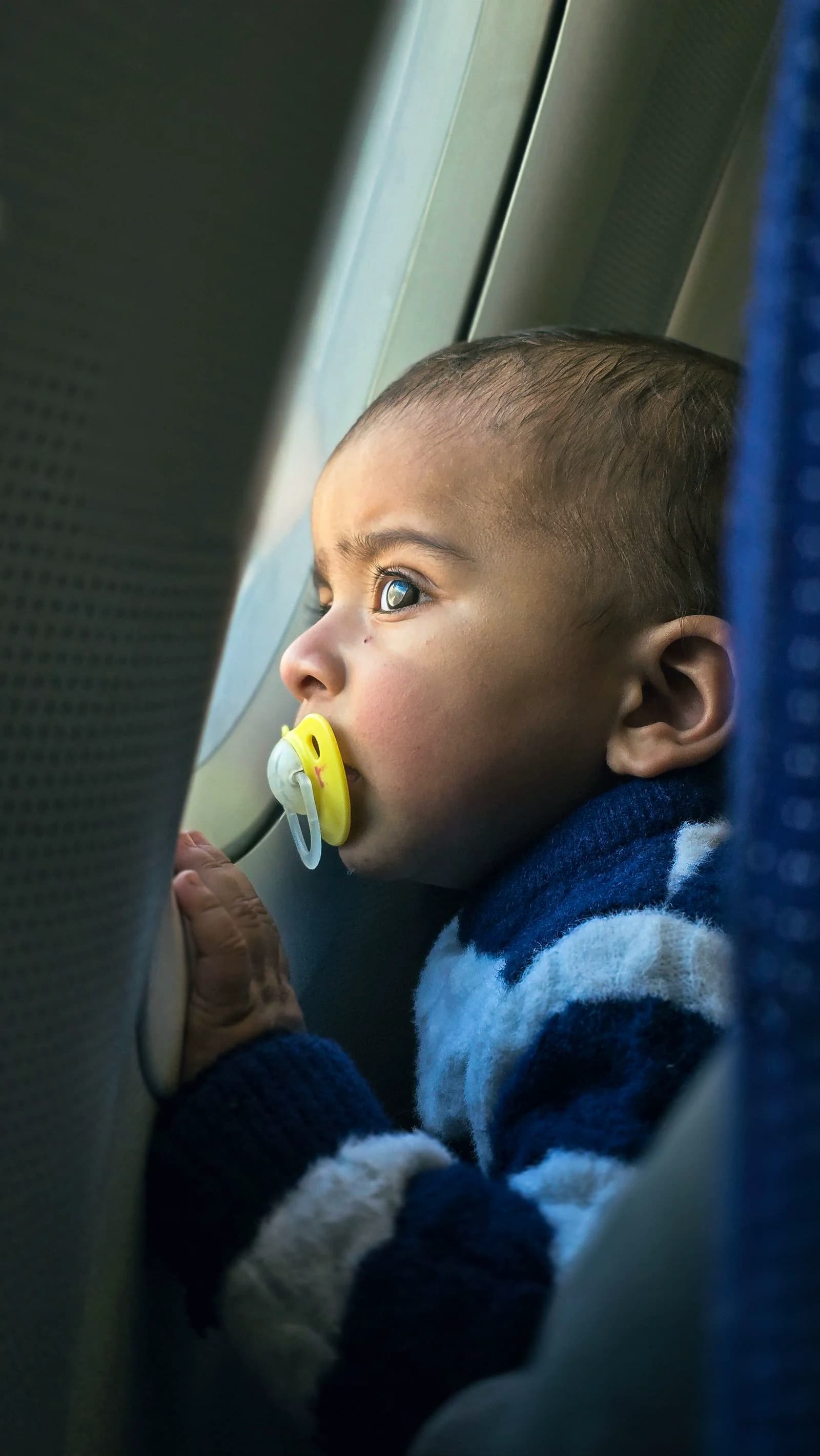 Baby with a pacifier gazing out of an airplane window during a flight