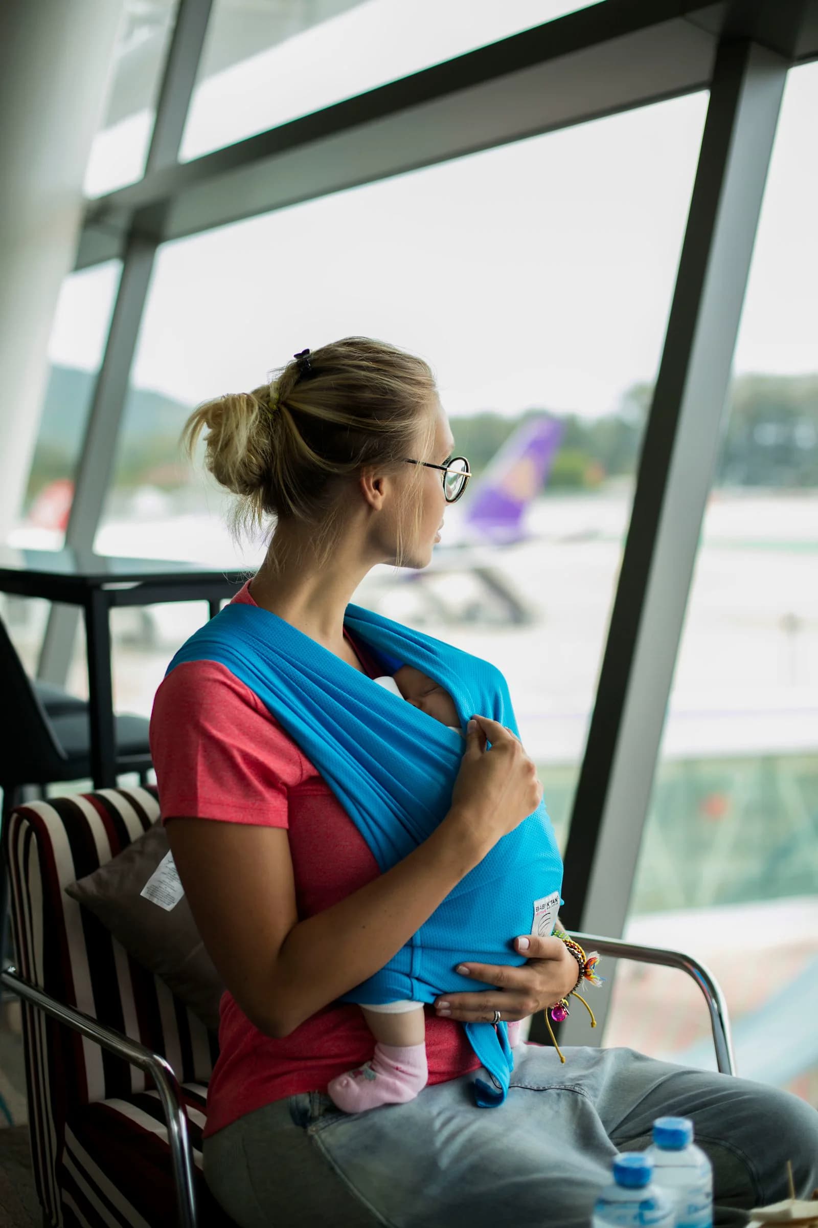 Mother with her baby in a sling waiting at the airport gate and watching the planes