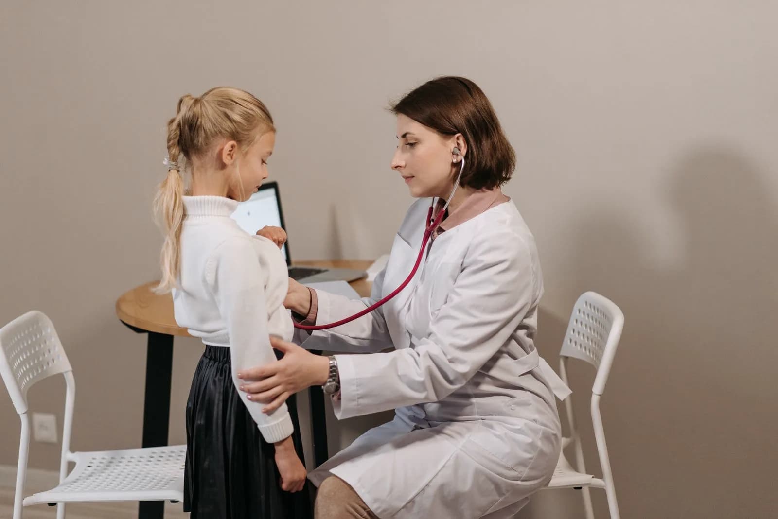Pediatrician examining a young child during a routine checkup while a parent watches nearby