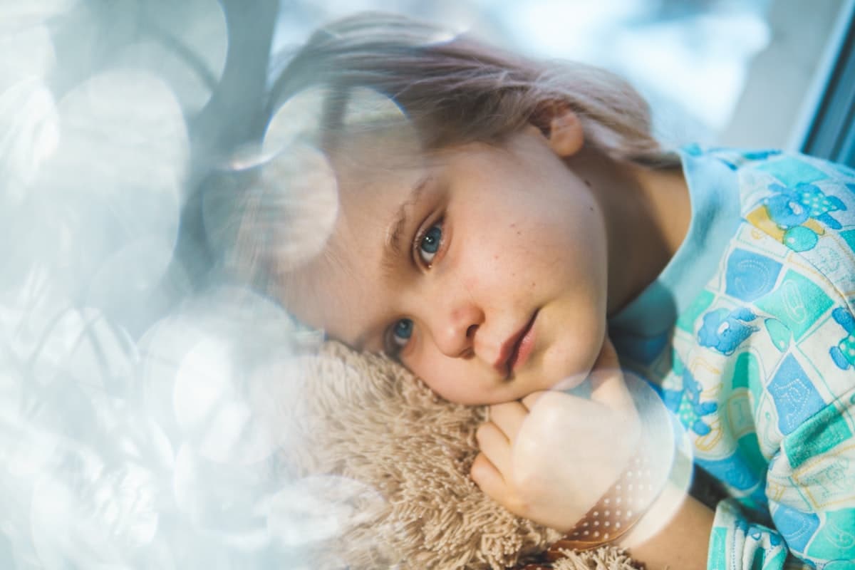 Child with fever lying on a bed with comfort toy, looking unwell
