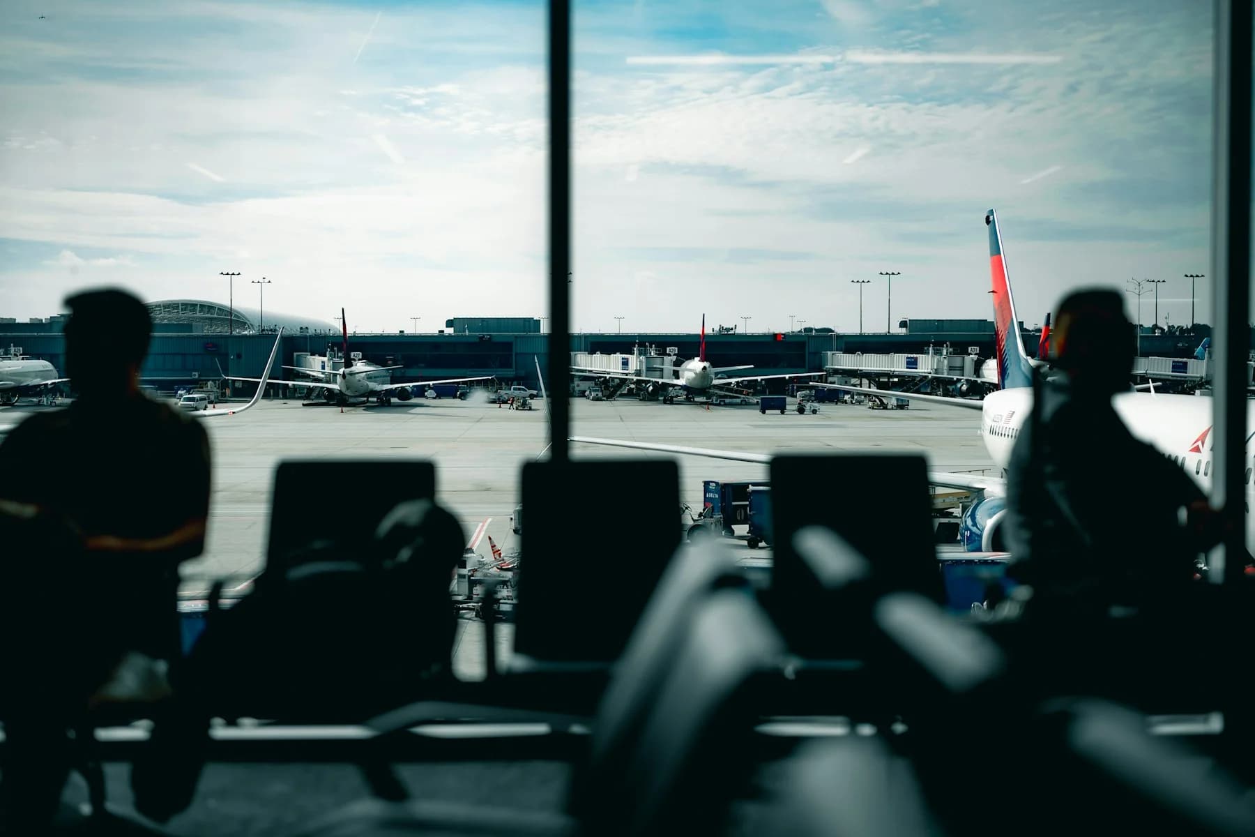 Tired parent sitting at airport gate with toddler, bags and snacks visible