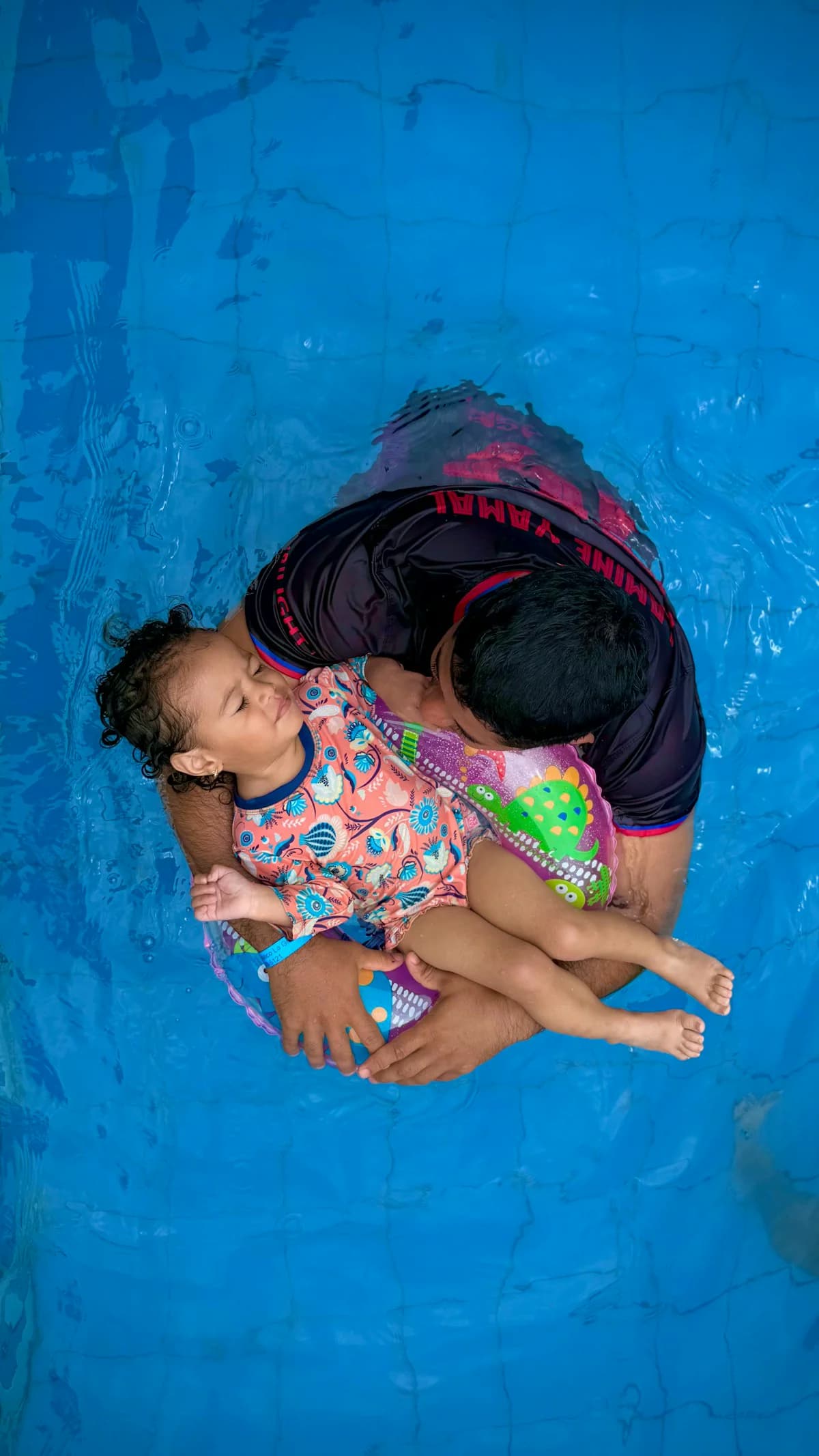 Parent and young child together in a swimming pool at the end of a happy summer day