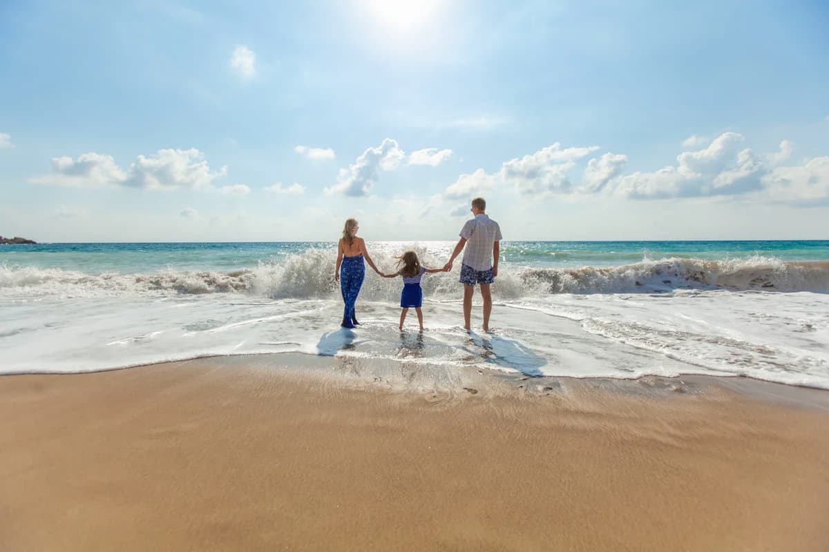 Parent and child walking hand-in-hand toward the ocean on a sunny beach day