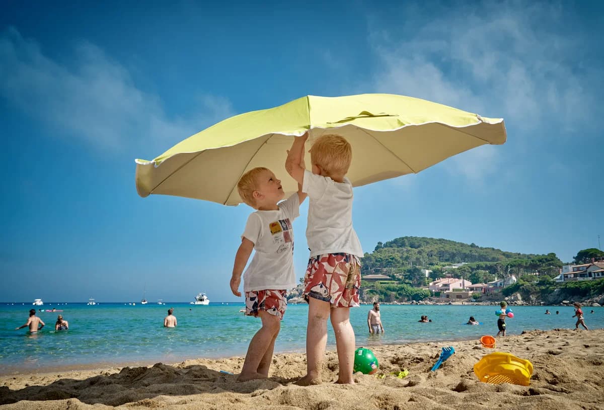Young children playing near a beach umbrella, taking a shade break from the sun